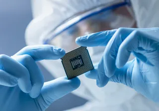 A photo of a person wearing rubber gloves, a face guard and protective overalls examining a microchip.