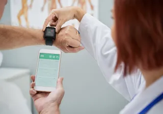 A patient and doctor are examining the readouts from a smartwatch and a smartphone.