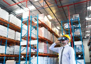 A photo of a person wearing a hard hat and a virtual reality headset in a warehouse.